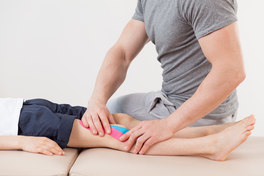 chiropractor adjusting a boy's knee with tape and massage